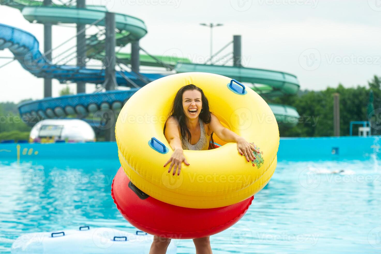 a woman in a swimsuit with rubber inflatable circles plays and has a good time near the pool of the summer water park photo