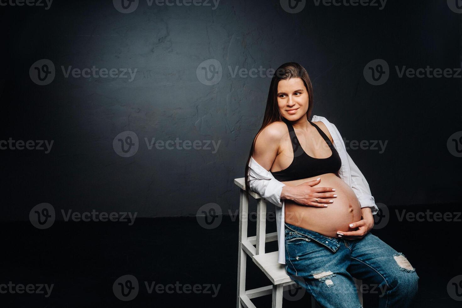 pregnant woman sitting on a ladder chair in a studio on a black background photo