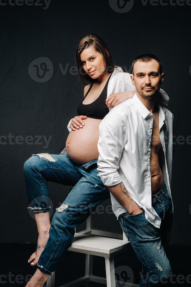 a pregnant woman and a man in a white shirt and jeans in a studio on a black background photo