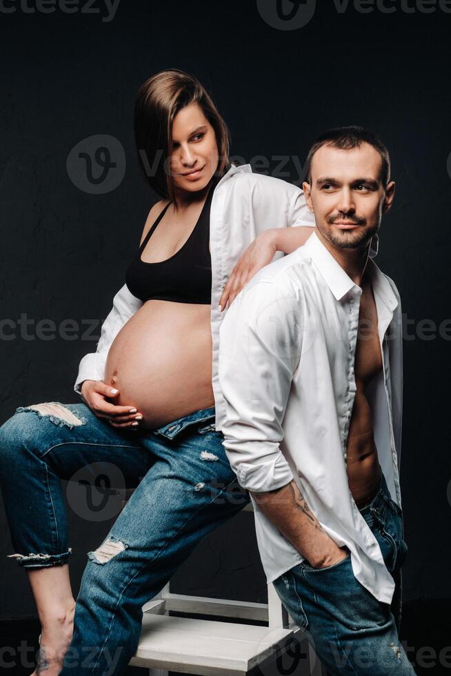 a pregnant woman and a man in a white shirt and jeans in a studio on a black background photo