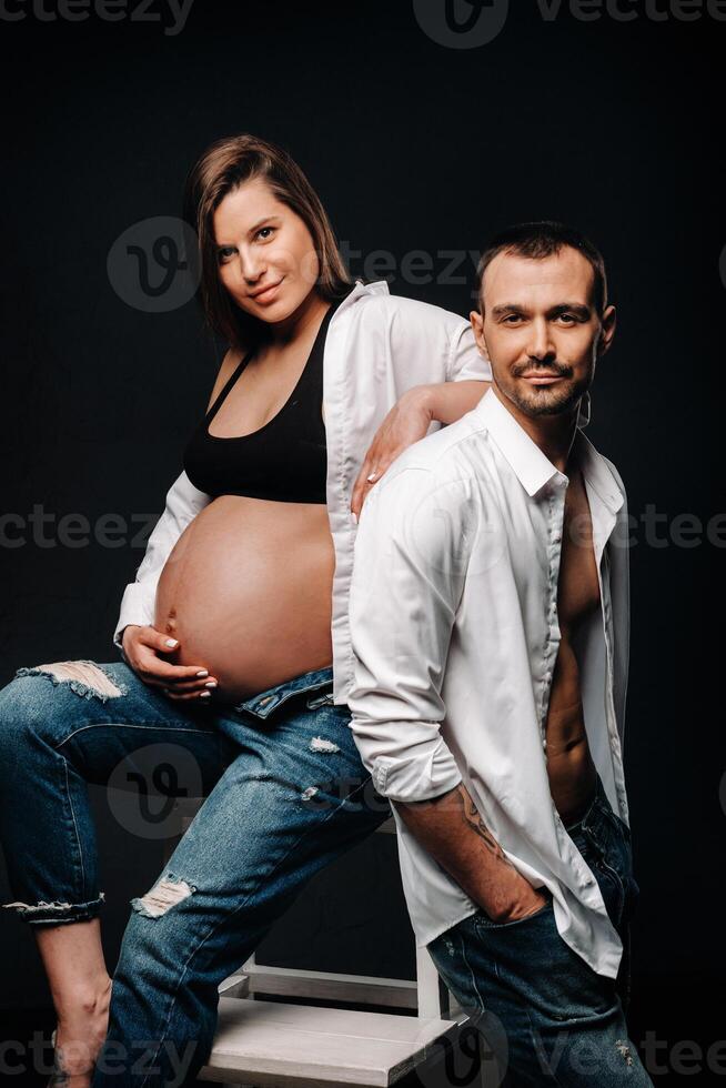 a pregnant woman and a man in a white shirt and jeans in a studio on a black background photo