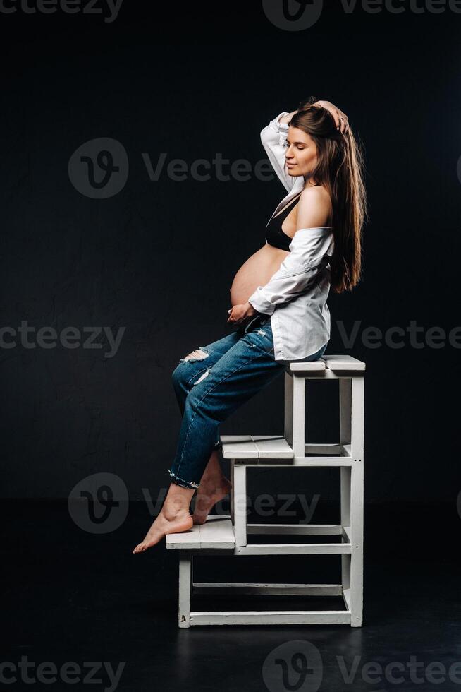 pregnant woman sitting on a ladder chair in a studio on a black background photo