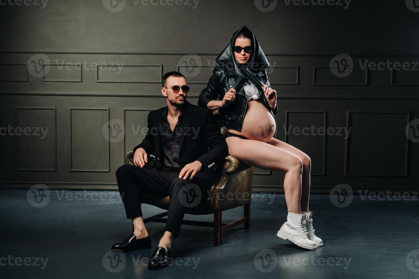 a pregnant woman in black clothes and a headscarf and a man in a suit in a studio on a dark background photo