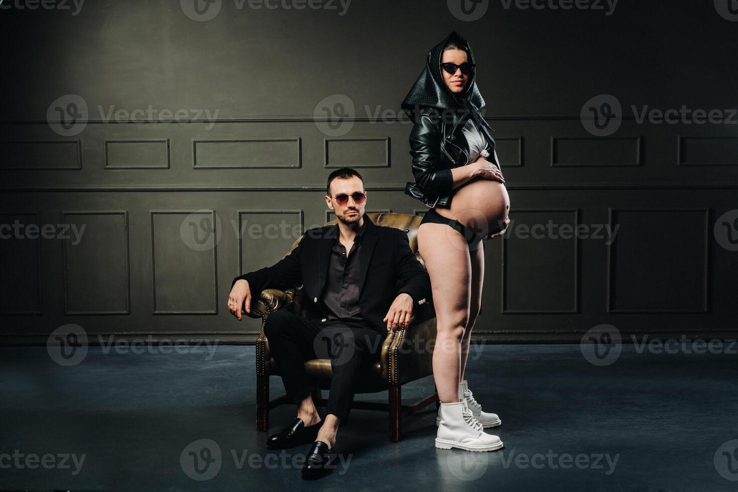 a pregnant woman in black clothes and a headscarf and a man in a suit in a studio on a dark background photo