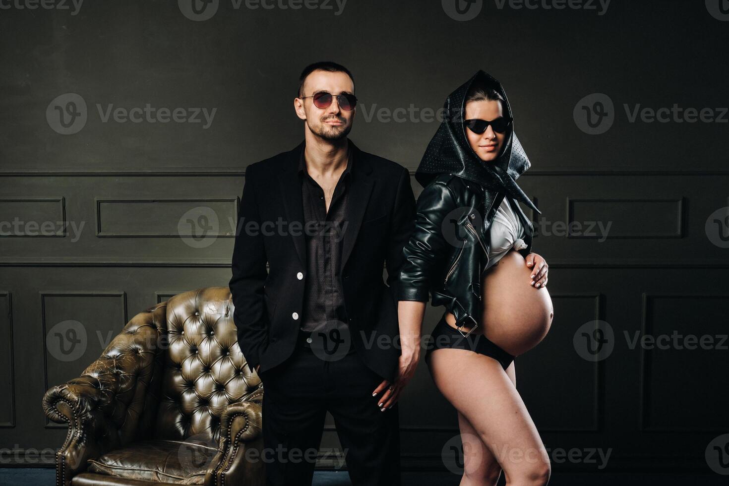 a pregnant woman in black clothes and a headscarf and a man in a suit in a studio on a dark background photo