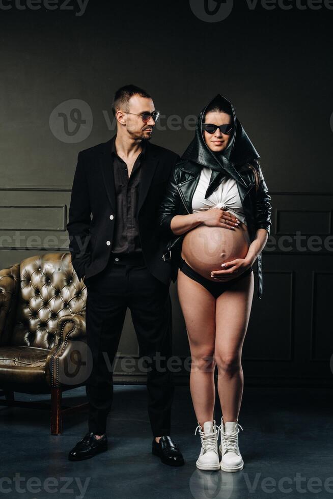 a pregnant woman in black clothes and a headscarf and a man in a suit in a studio on a dark background photo