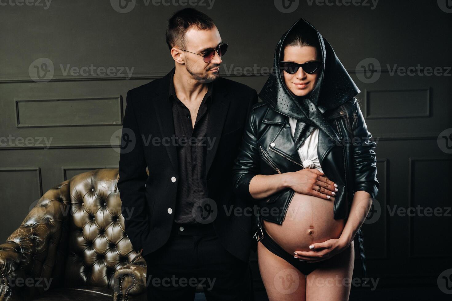a pregnant woman in black clothes and a headscarf and a man in a suit in a studio on a dark background photo