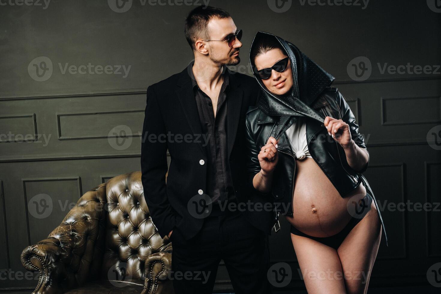 a pregnant woman in black clothes and a headscarf and a man in a suit in a studio on a dark background photo