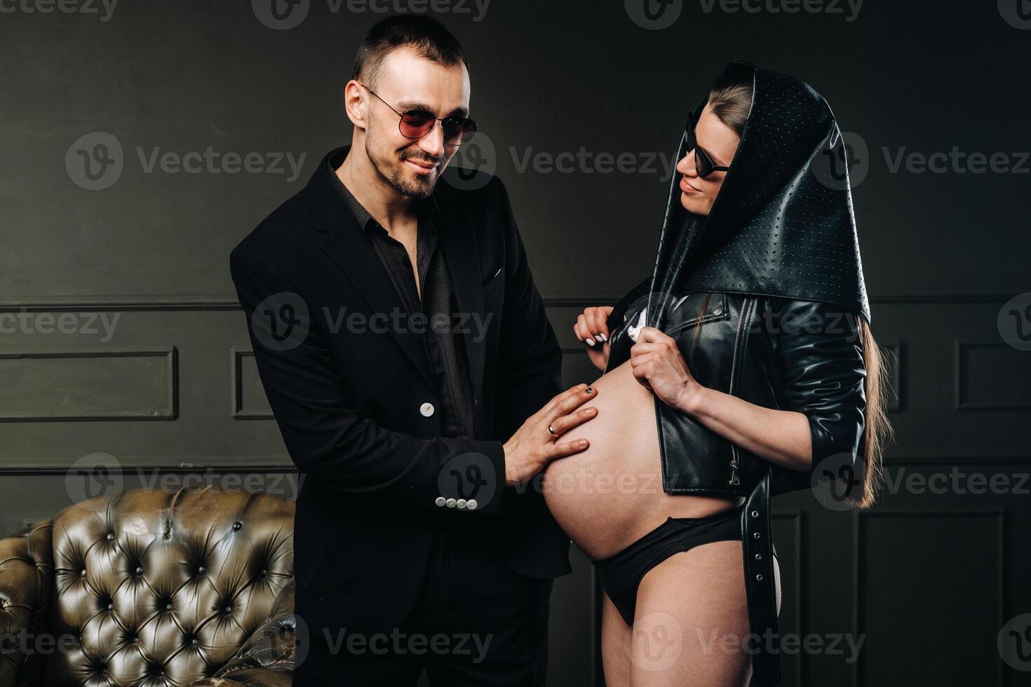 a pregnant woman in black clothes and a headscarf and a man in a suit in a studio on a dark background photo