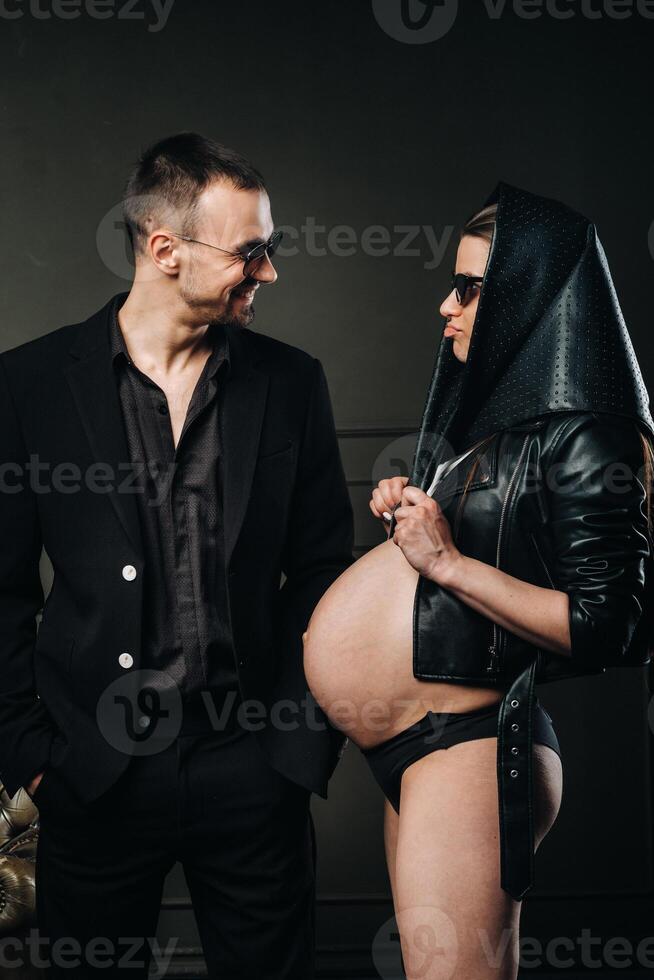 a pregnant woman in black clothes and a headscarf and a man in a suit in a studio on a dark background photo