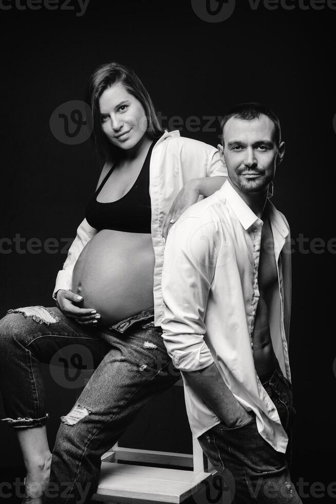 a pregnant woman and a man in a white shirt and jeans in a studio on a black background photo