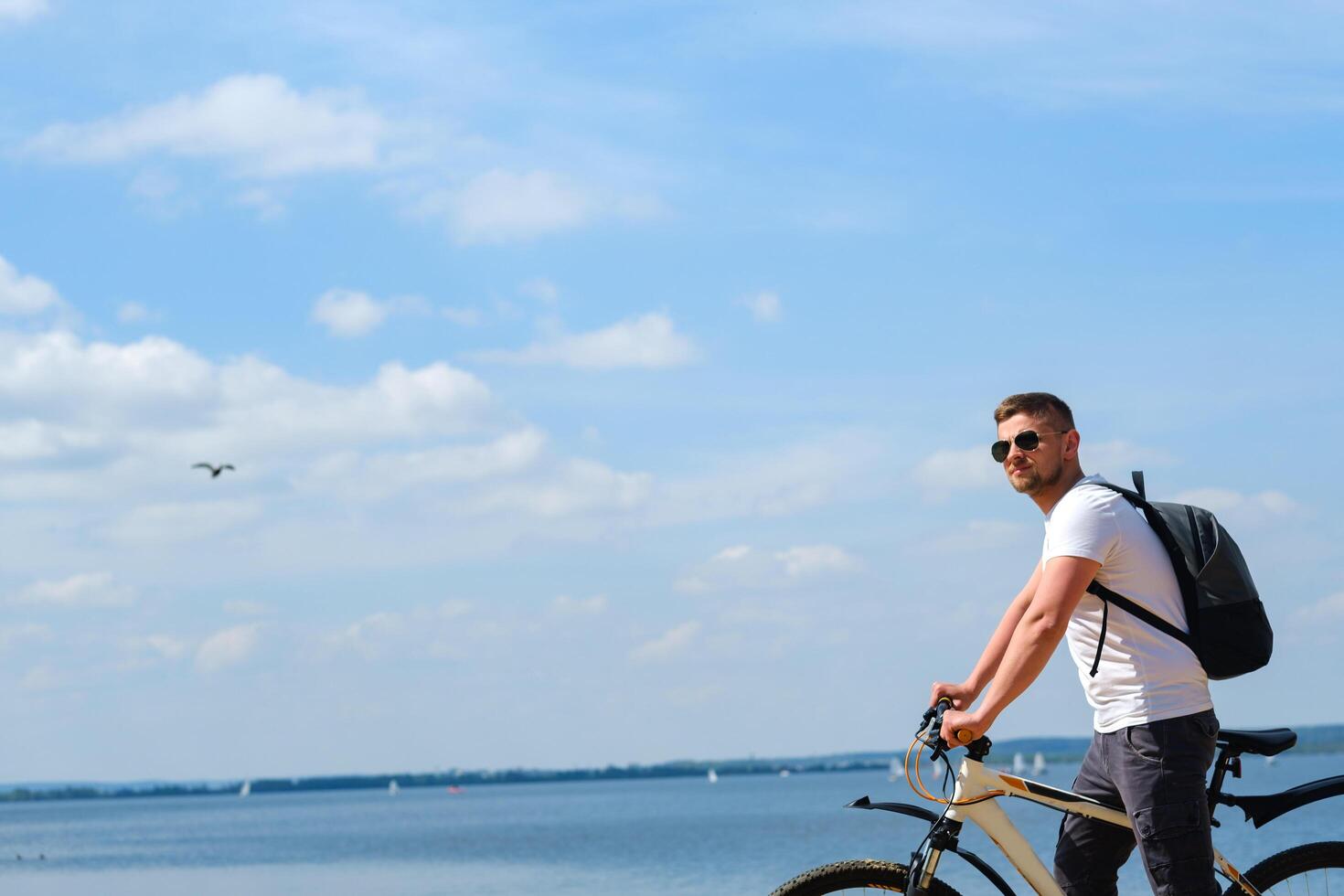 A cyclist with a backpack and glasses rides along the sea on a bicycle on a beautiful sunny day photo