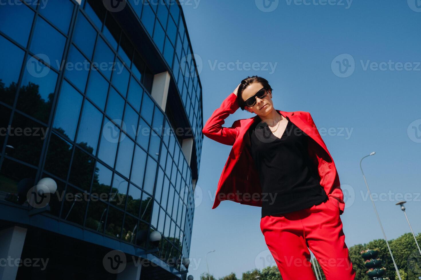 A girl in a red suit stands against the background of a modern building in the city photo