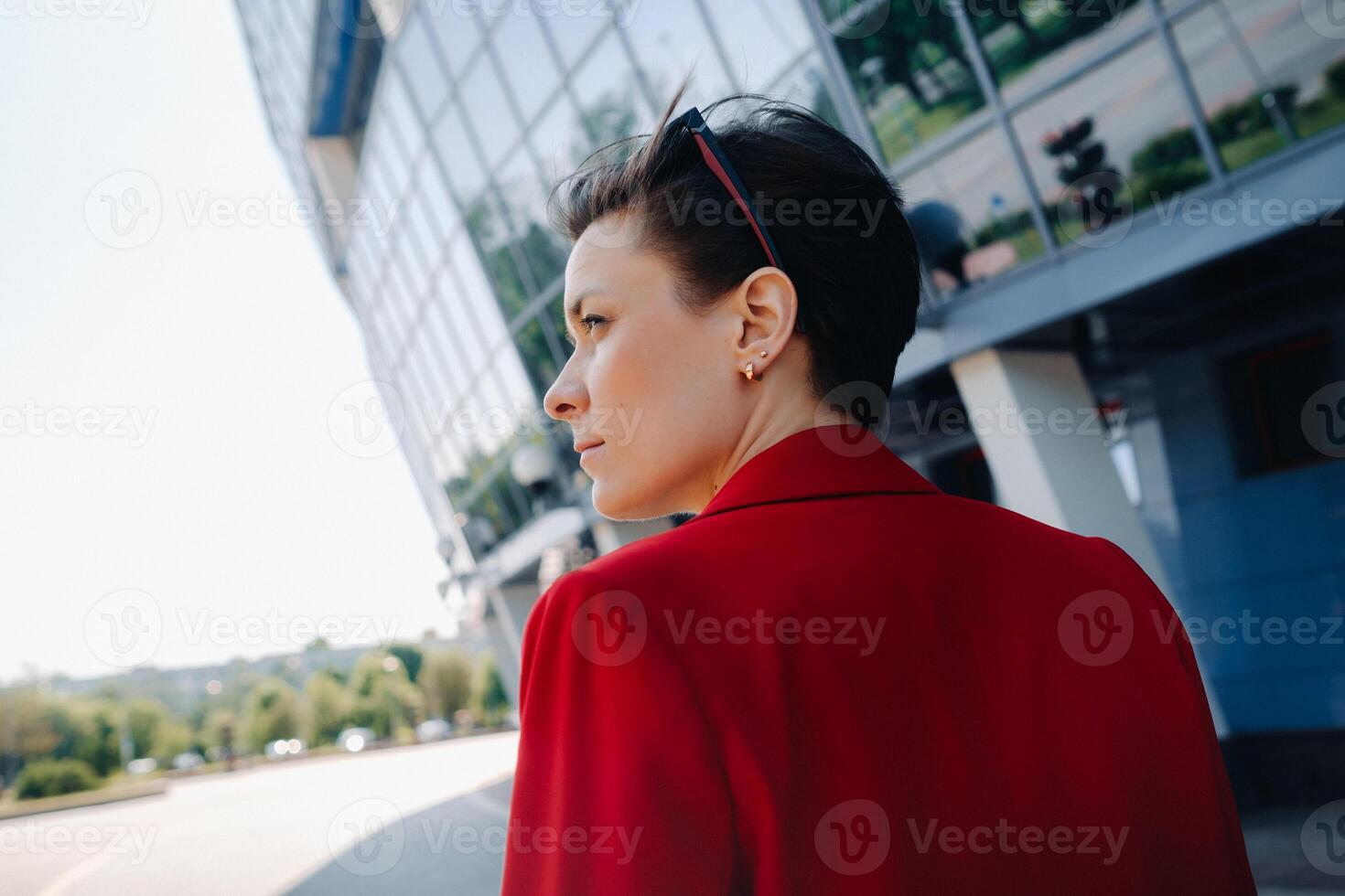 A girl in a red suit stands against the background of a modern building in the city photo
