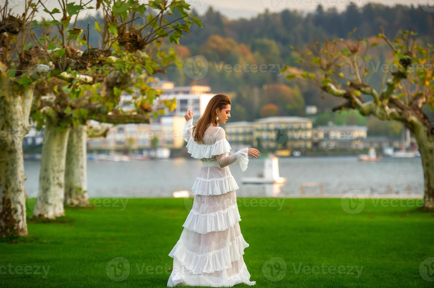 A bride in a white wedding dress in a park in an Austrian town with large trees at sunset photo