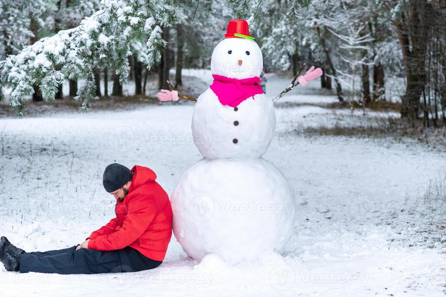 A man sleeps near a large snowman in a snow-covered forest photo