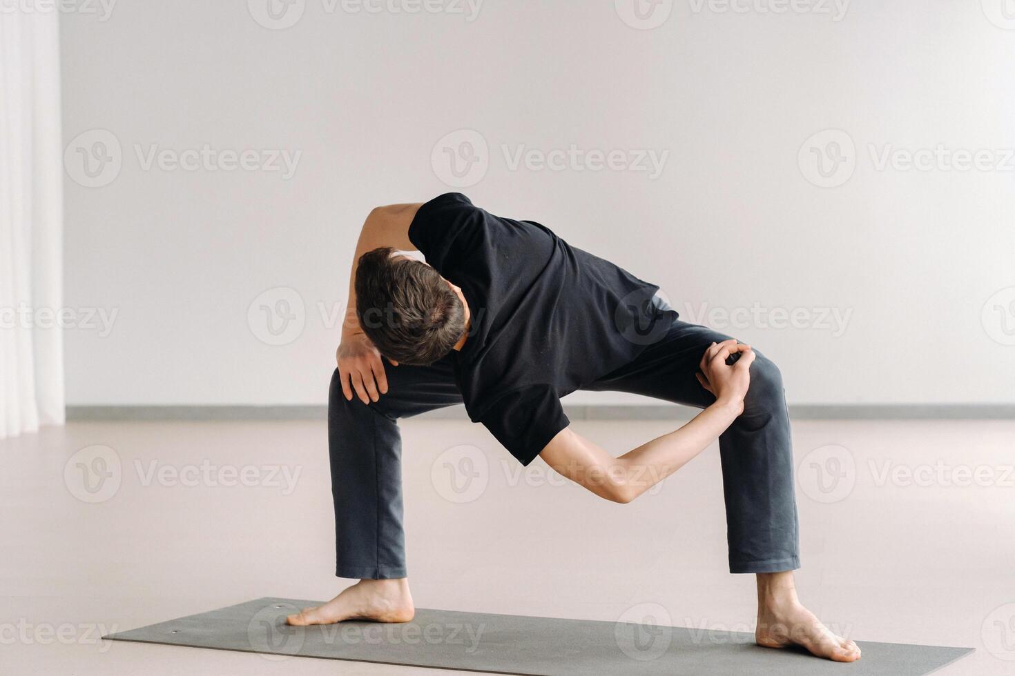 A man in a black T-shirt trains standing up, doing stretching in the gym photo