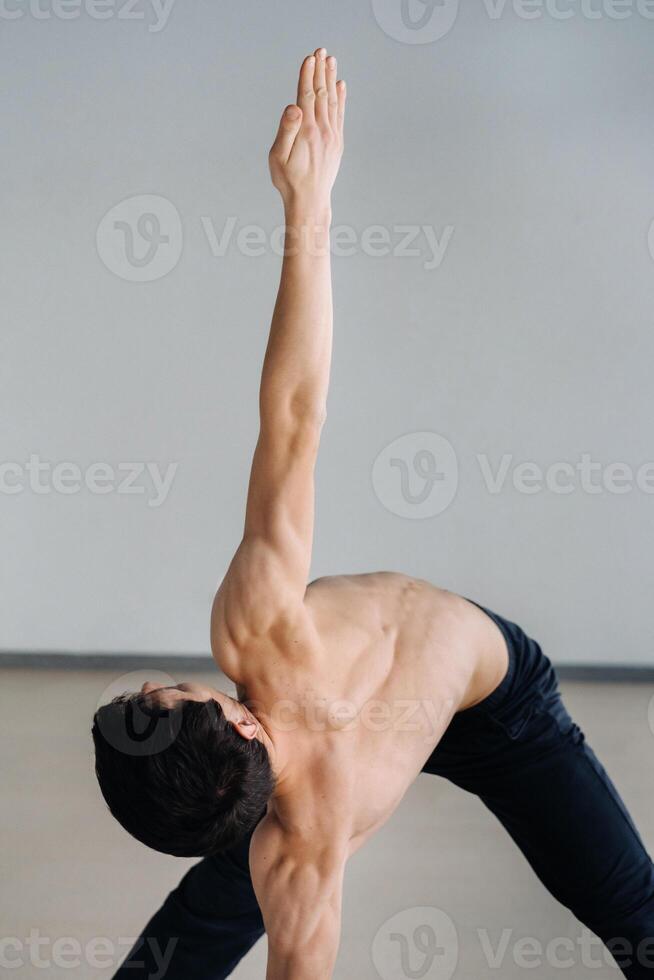 A man with a bare torso trains standing up, doing stretching in the gym photo