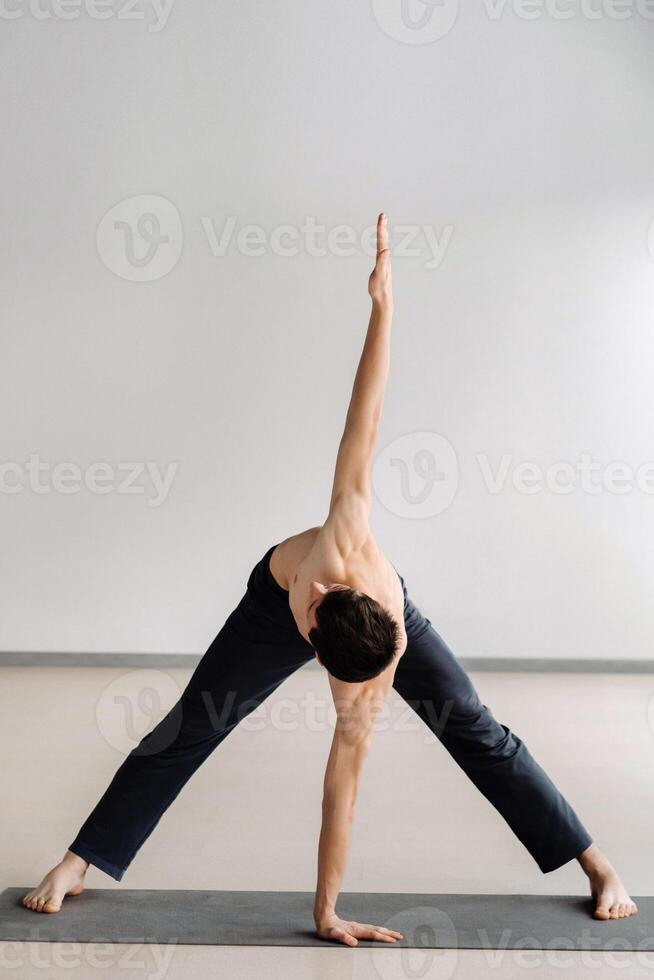 A man with a bare torso trains standing up, doing stretching in the gym photo