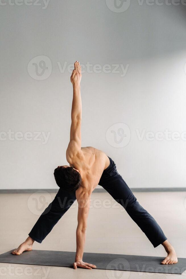 A man with a bare torso trains standing up, doing stretching in the gym photo