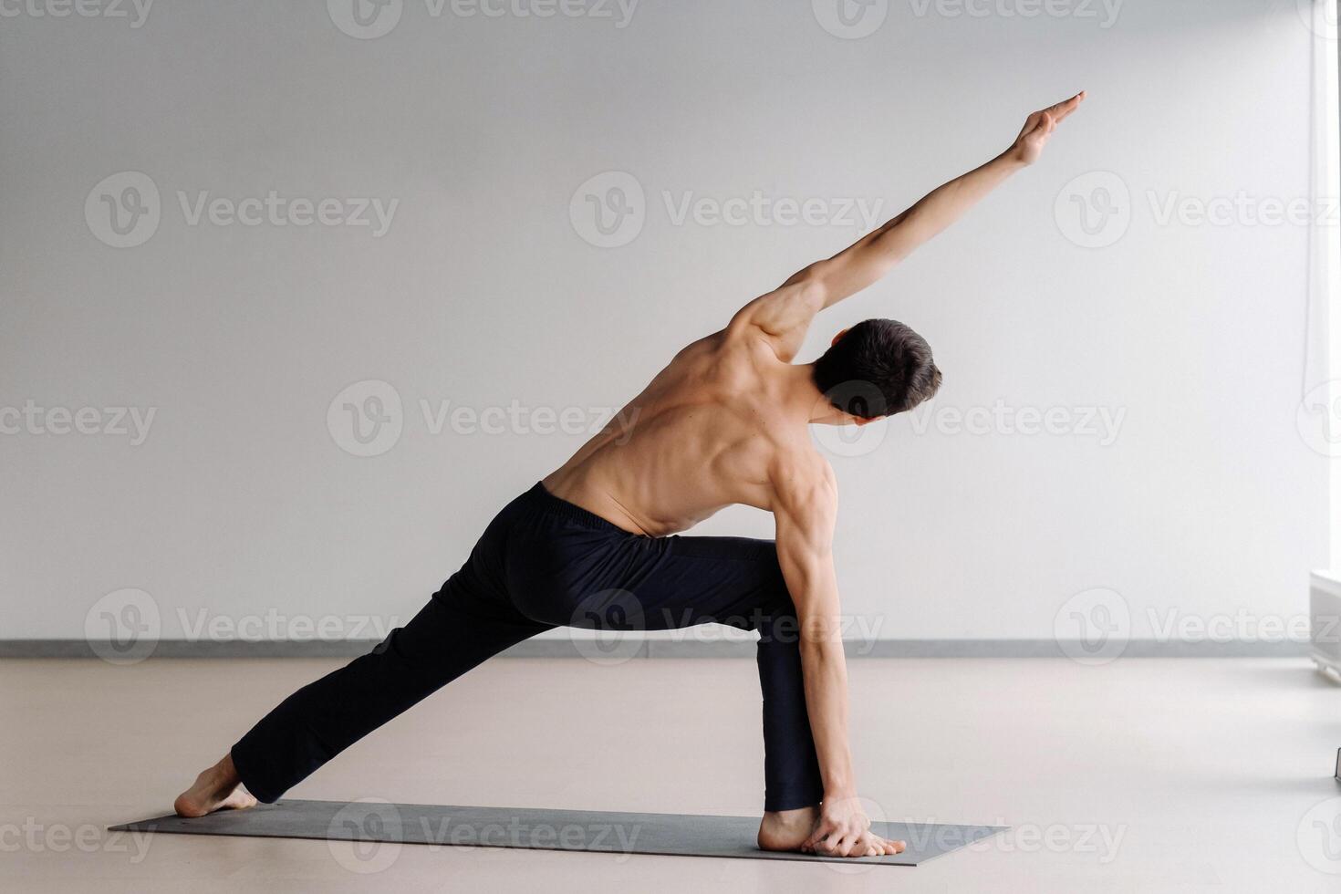 A man with a bare torso trains standing up, doing stretching in the gym photo