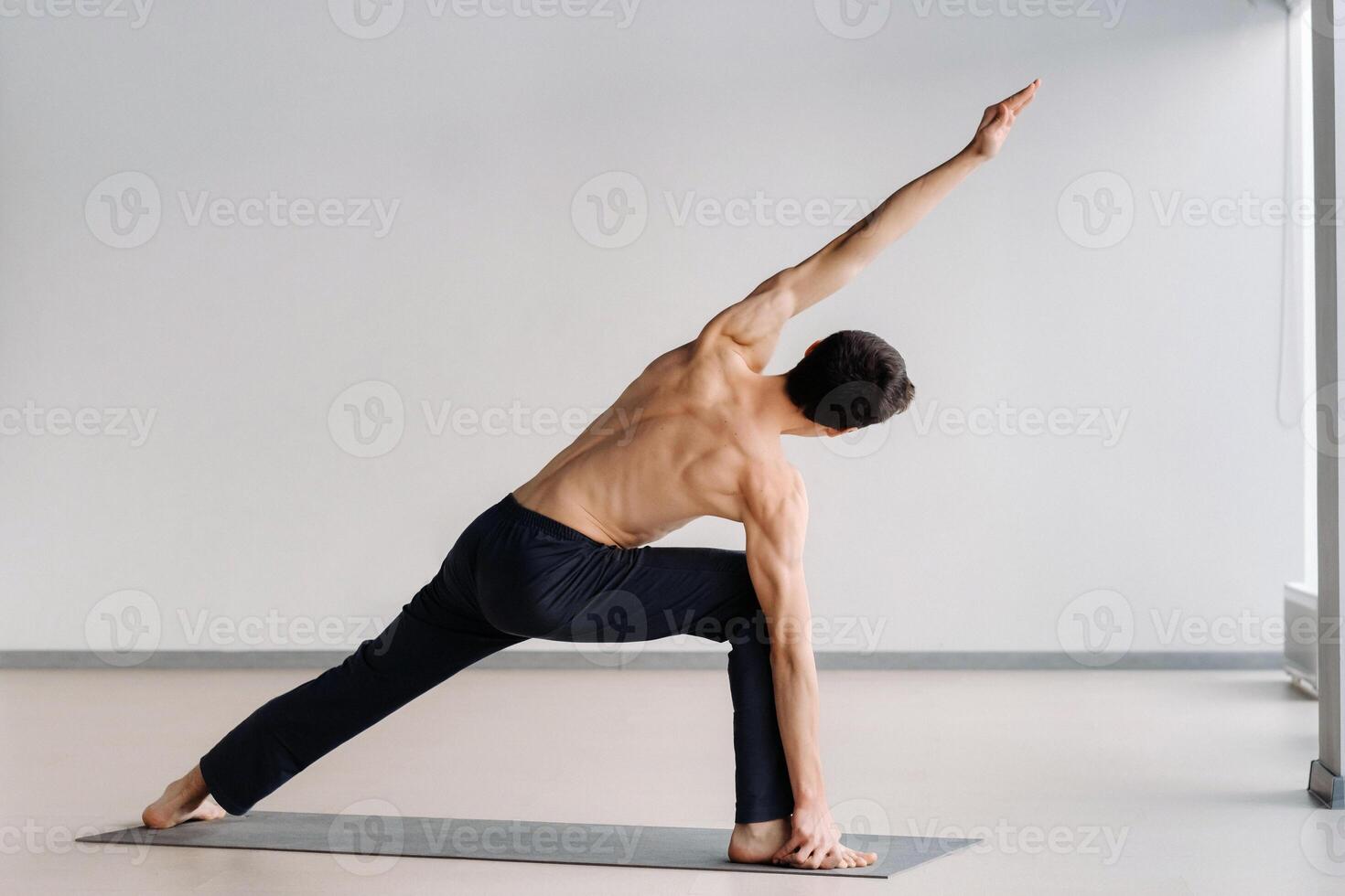 A man with a bare torso trains standing up, doing stretching in the gym photo