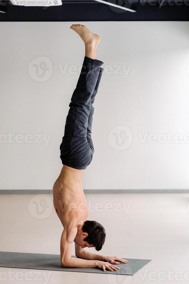 A man with a bony torso trains standing on his hands in the gym photo
