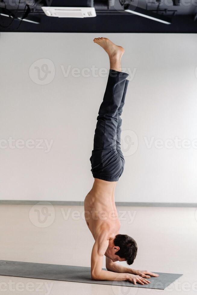 A man with a bony torso trains standing on his hands in the gym photo