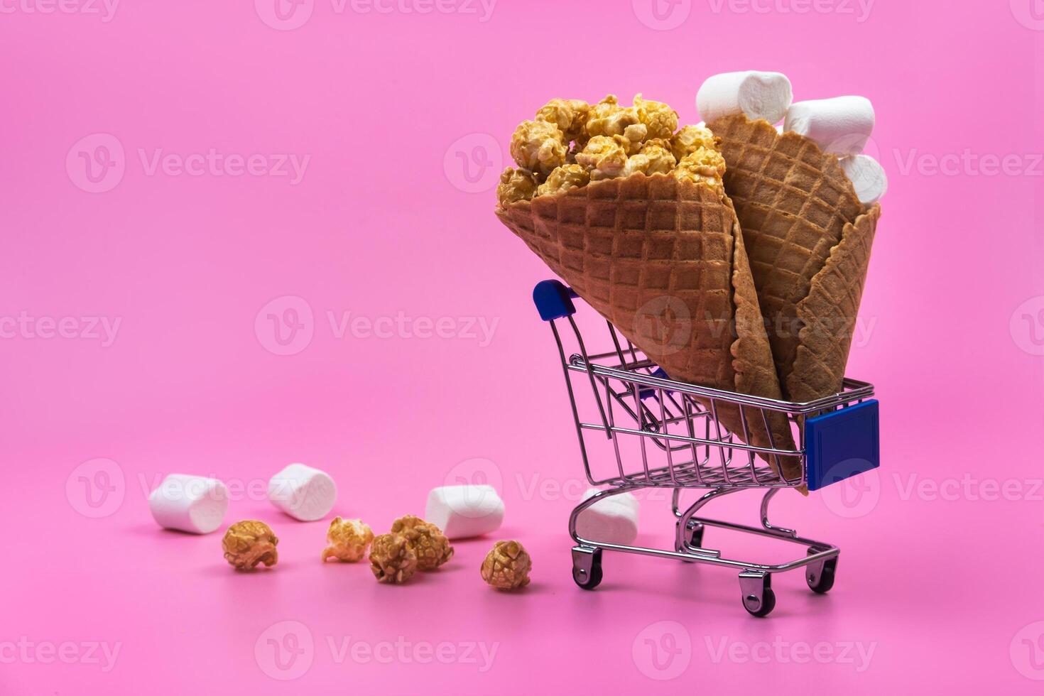 Shopping cart with ice cream cones with sweets on a pink background photo
