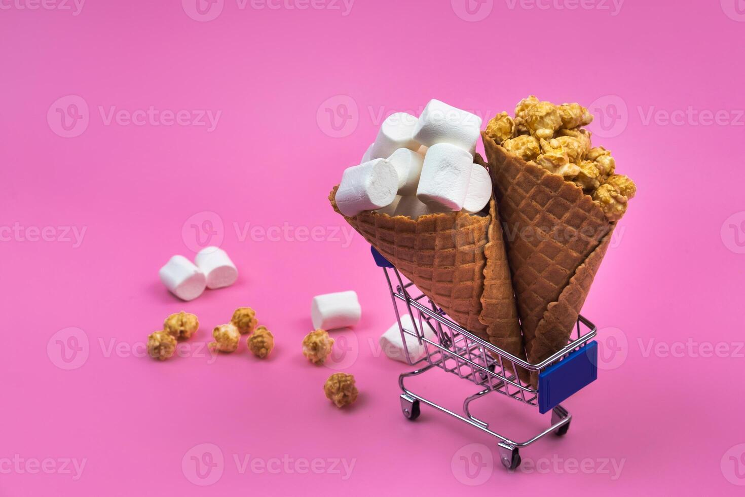 Shopping cart with ice cream cones with sweets on a pink background photo