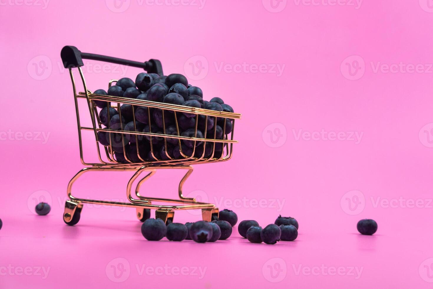 Blueberries in a grocery cart on a pink background. Scattered blueberries near a grocery cart on a pink background. photo