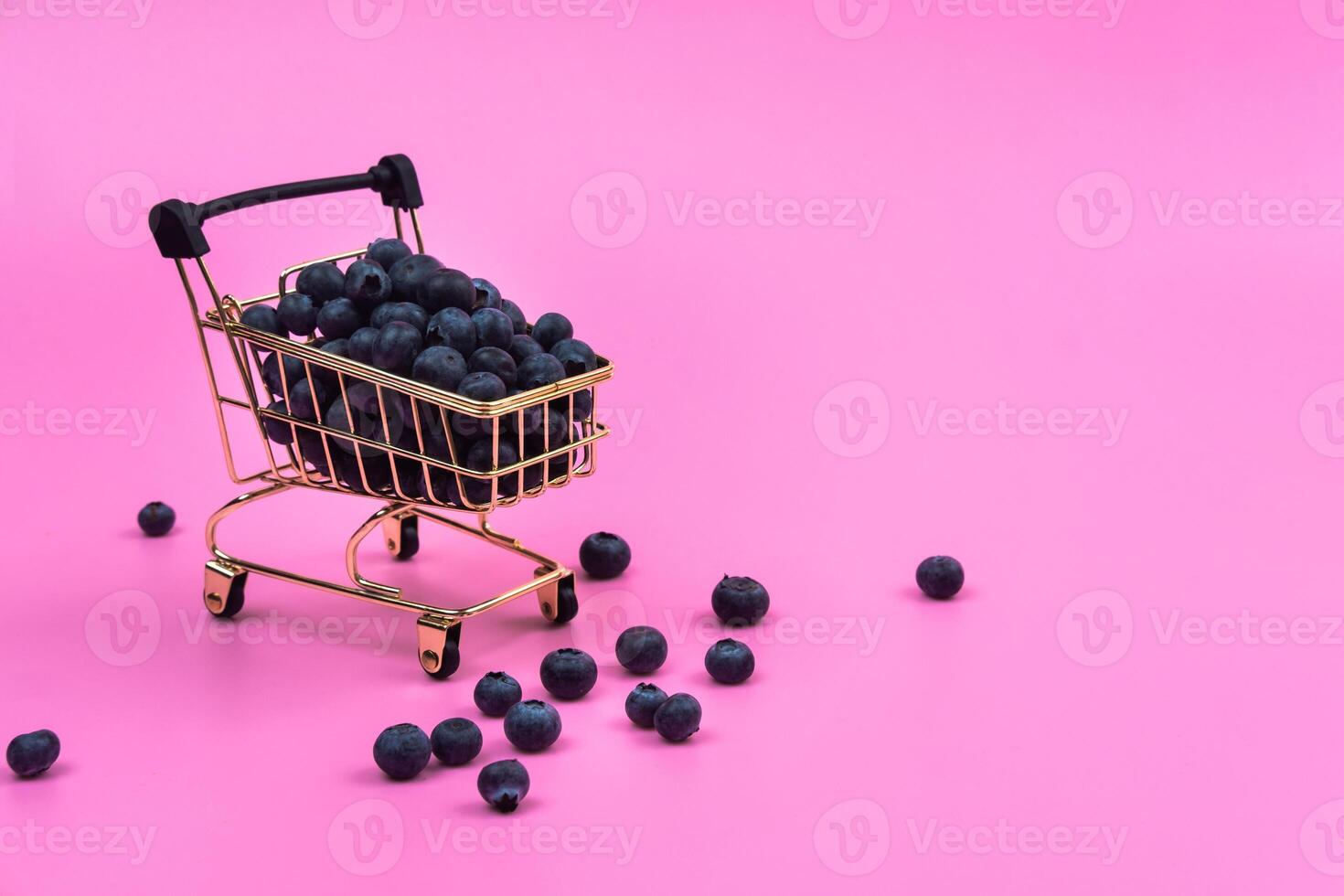 Blueberries in a grocery cart on a pink background. Scattered blueberries near a grocery cart on a pink background. photo