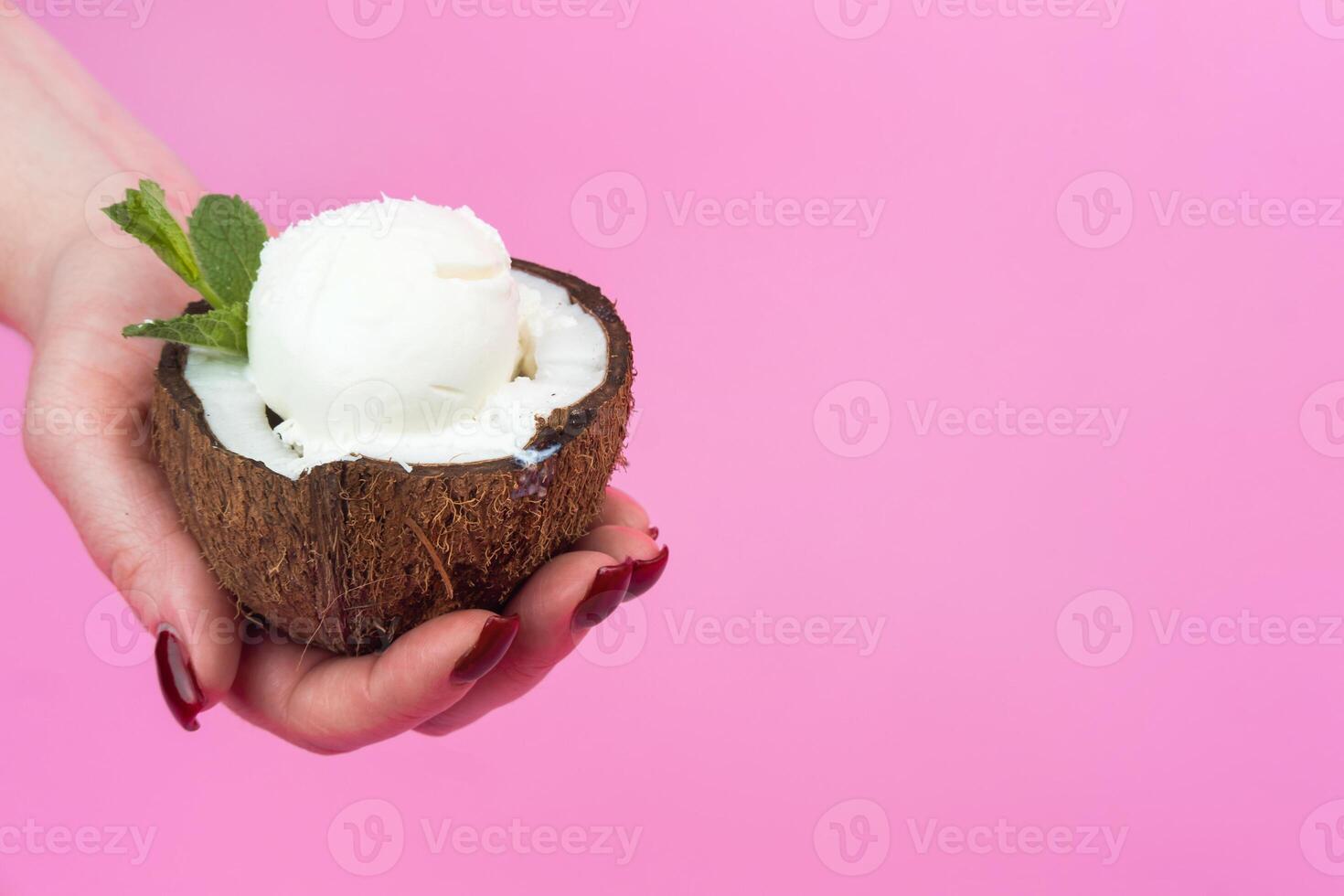 Vanilla ice cream balls in a fresh coconut half, decorated with mint leaves in your hand on a pink background photo