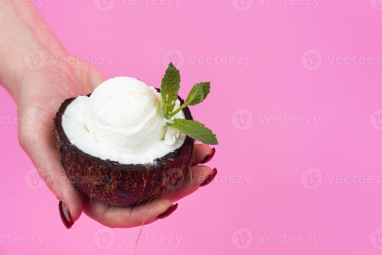 Vanilla ice cream balls in a fresh coconut half, decorated with mint leaves in your hand on a pink background photo
