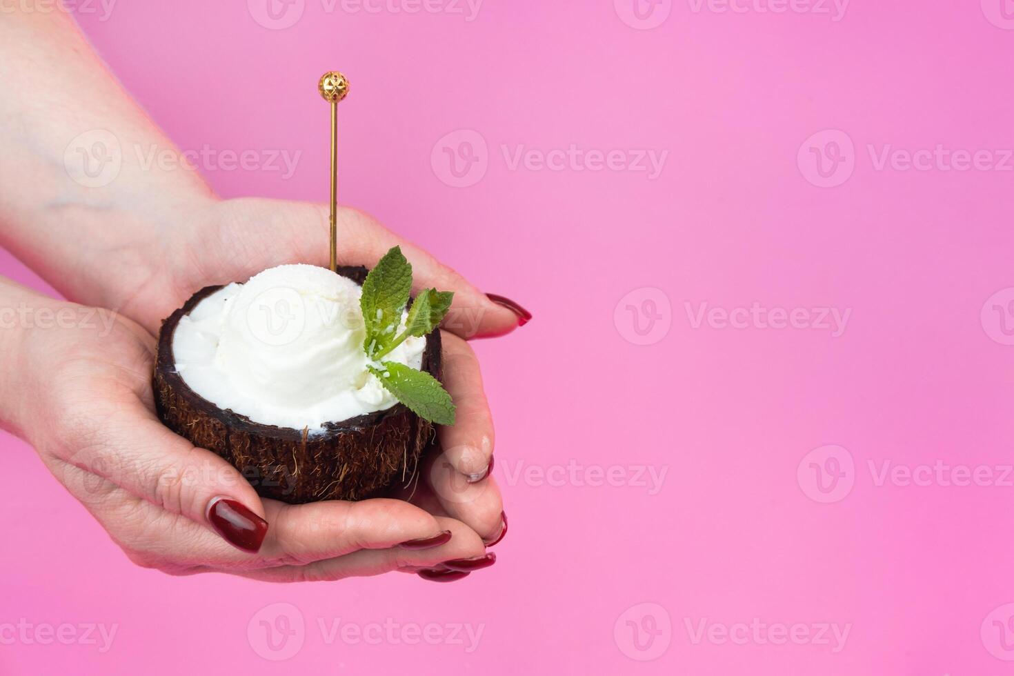 Vanilla ice cream balls in a fresh coconut half, decorated with mint leaves in the hand with a spoon on a pink background photo