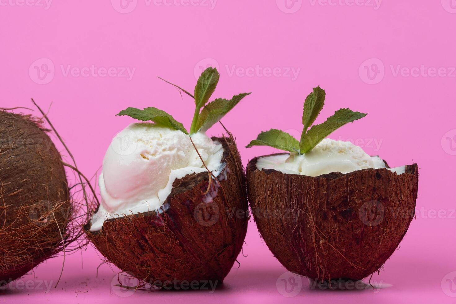 Vanilla ice cream balls in fresh coconut halves decorated with mint leaves on a pink background photo