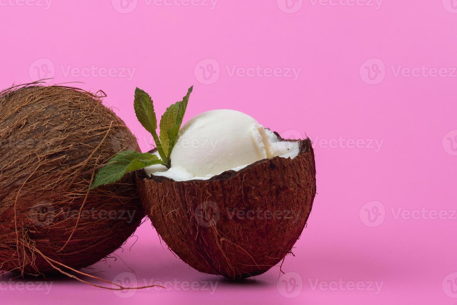 Vanilla ice cream balls in fresh coconut halves decorated with mint leaves on a pink background photo