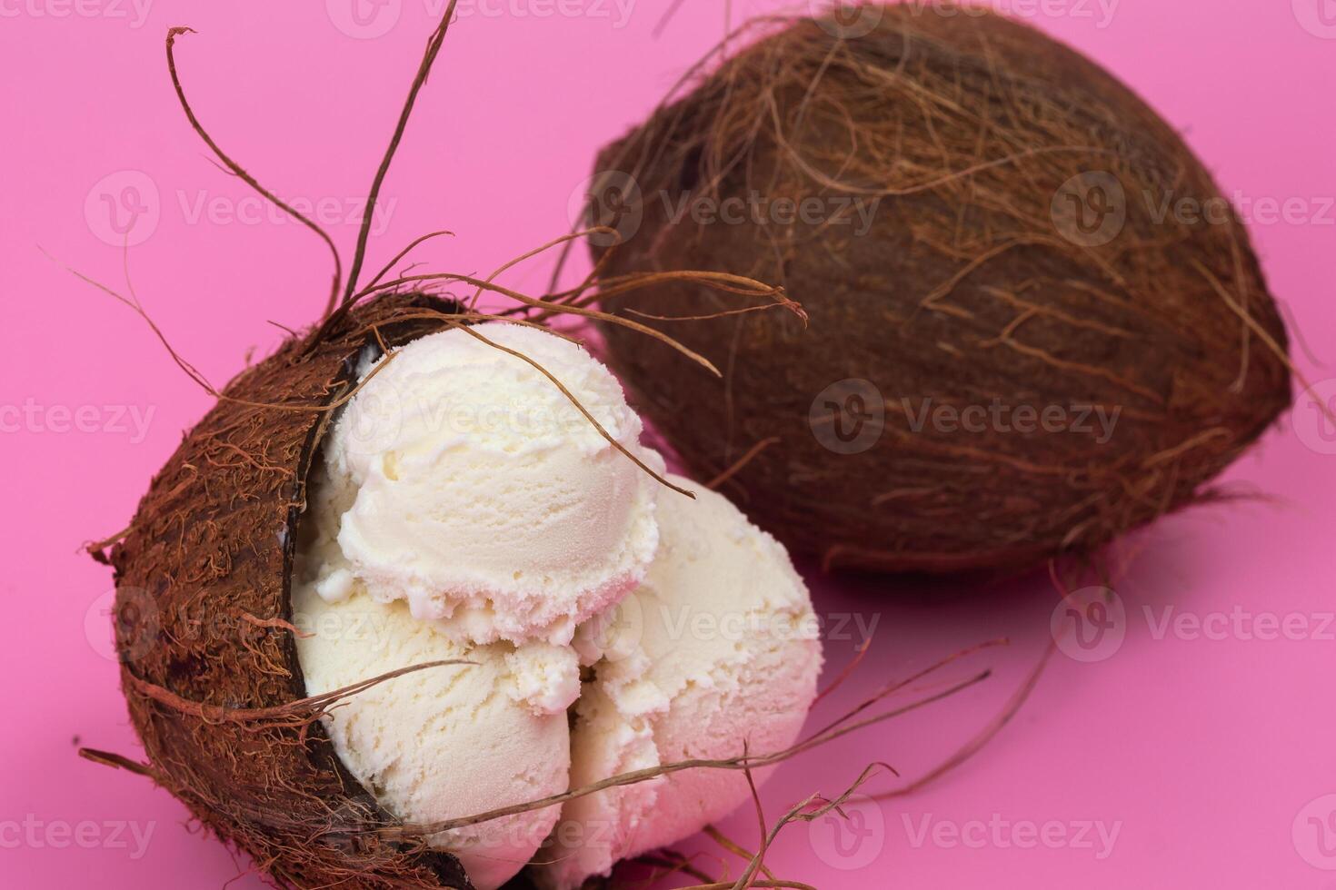 Vanilla ice cream balls in an empty coconut decorated with mint leaves on a pink background photo