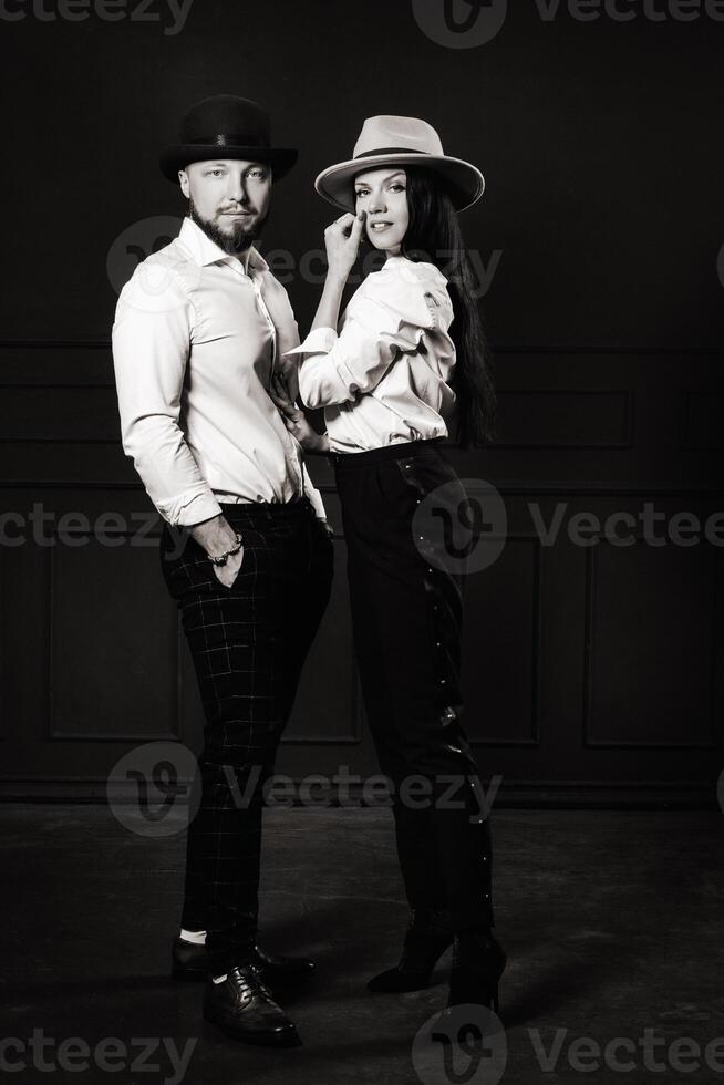 A man and a woman in white shirts and hats on a black background.A couple in love poses in the interior of the studio. black and white photo