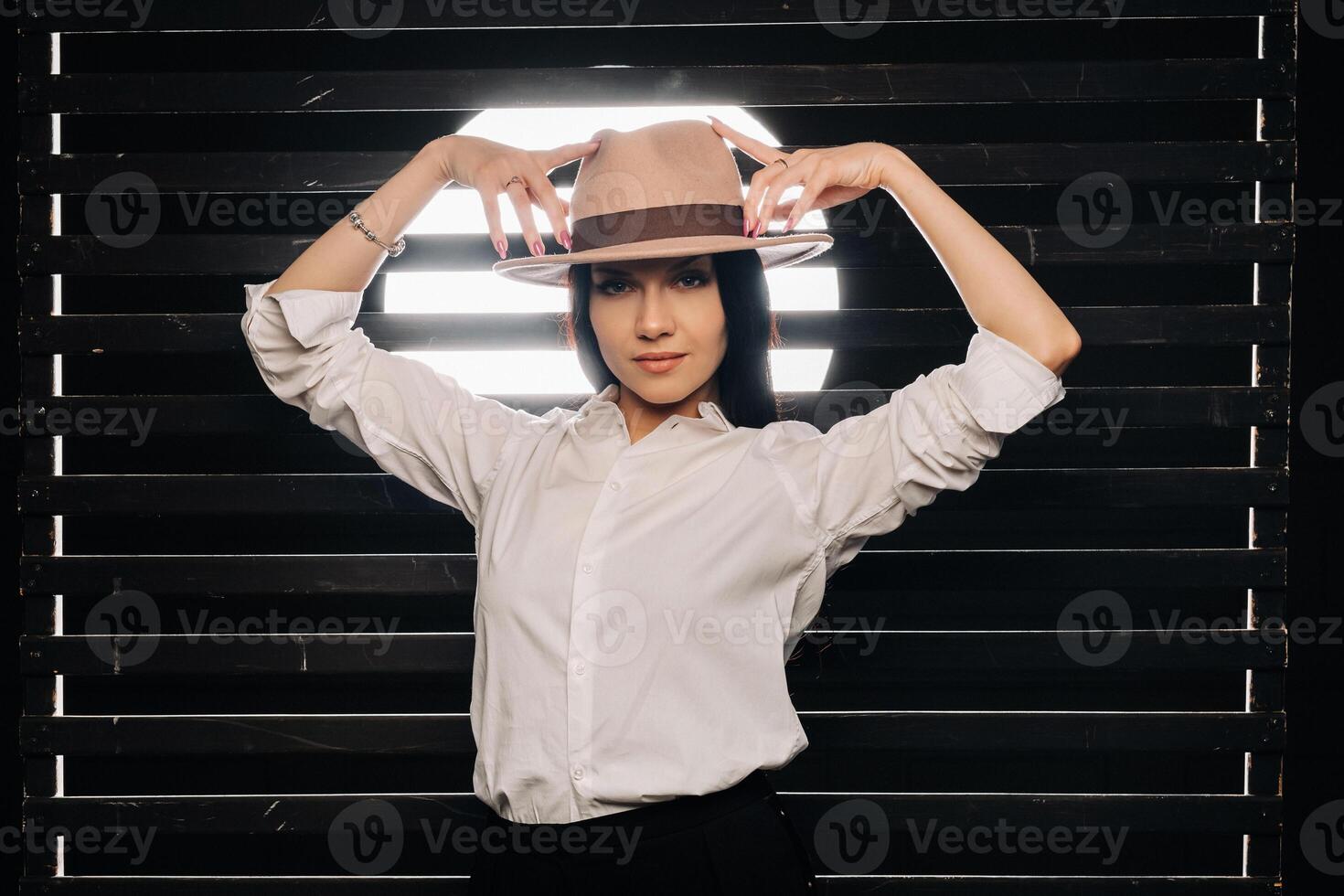 Elegant brunette girl in a white shirt and beige hat on a dark background photo