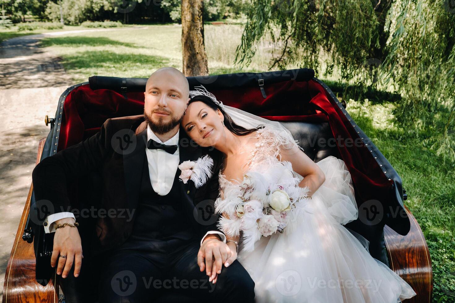 The bride and groom with a bouquet are sitting in a carriage in nature in retro style photo