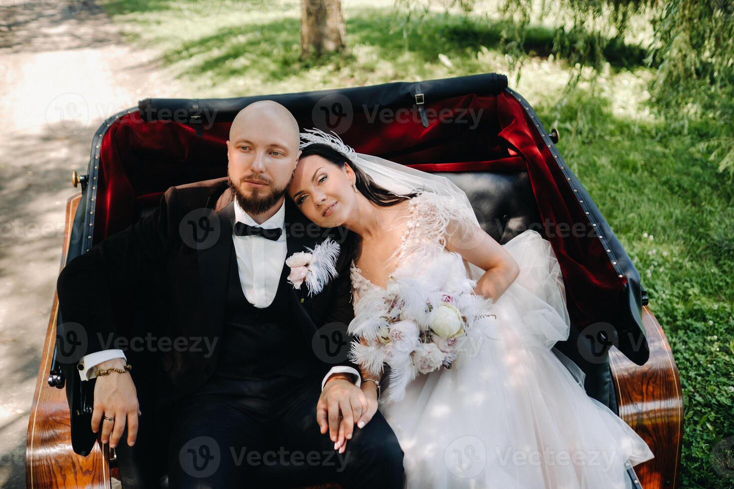 The bride and groom with a bouquet are sitting in a carriage in nature in retro style photo
