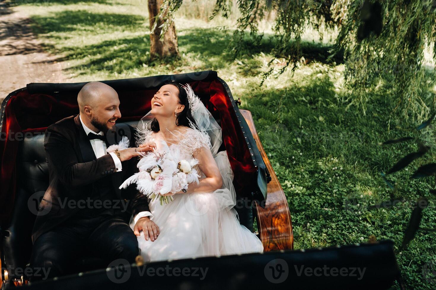 The bride and groom with a bouquet are sitting in a carriage in nature in retro style photo
