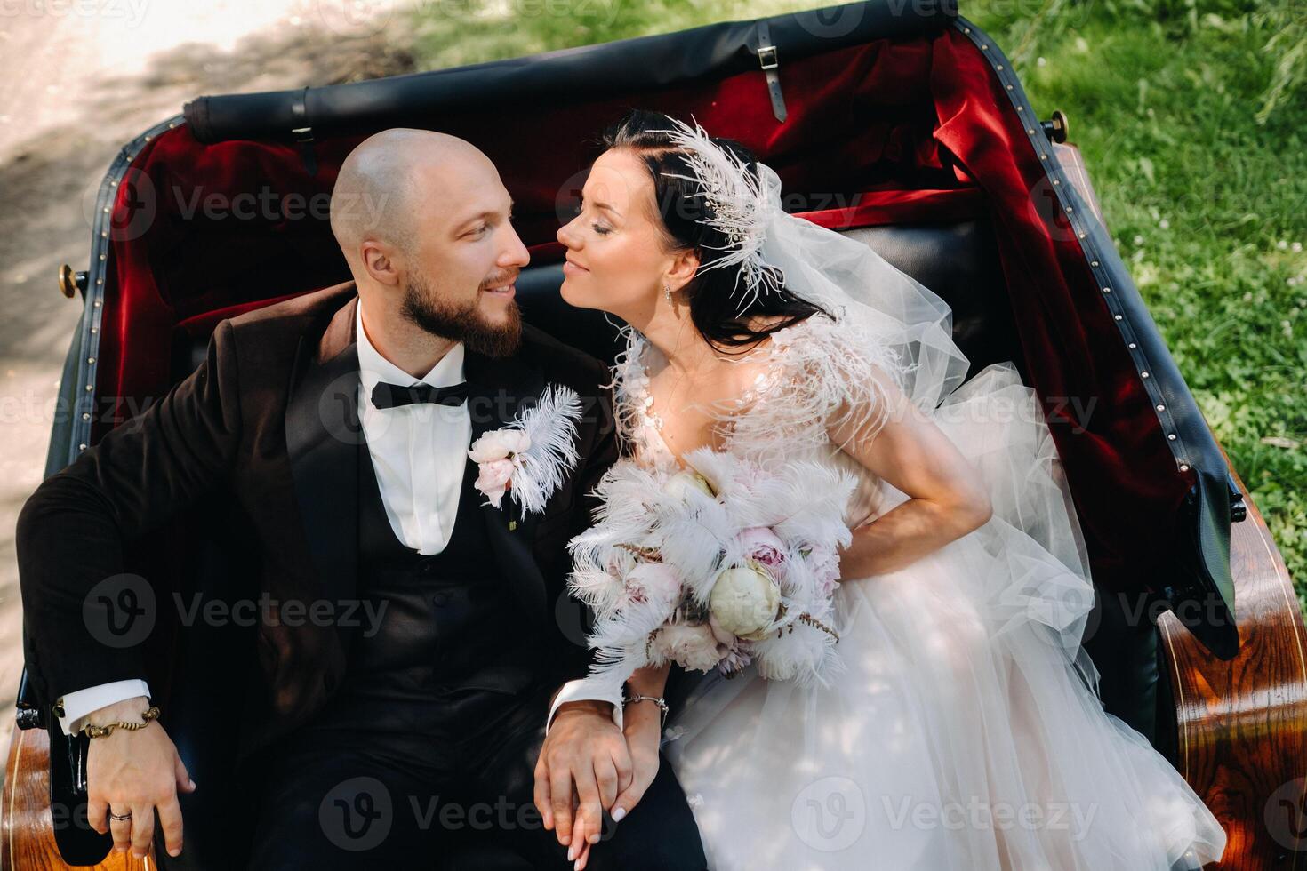 The bride and groom with a bouquet are sitting in a carriage in nature in retro style photo