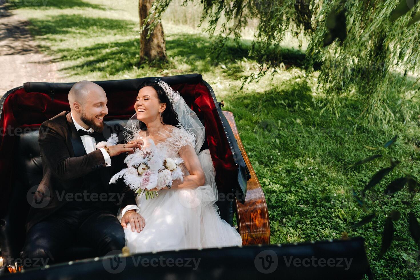 The bride and groom with a bouquet are sitting in a carriage in nature in retro style photo