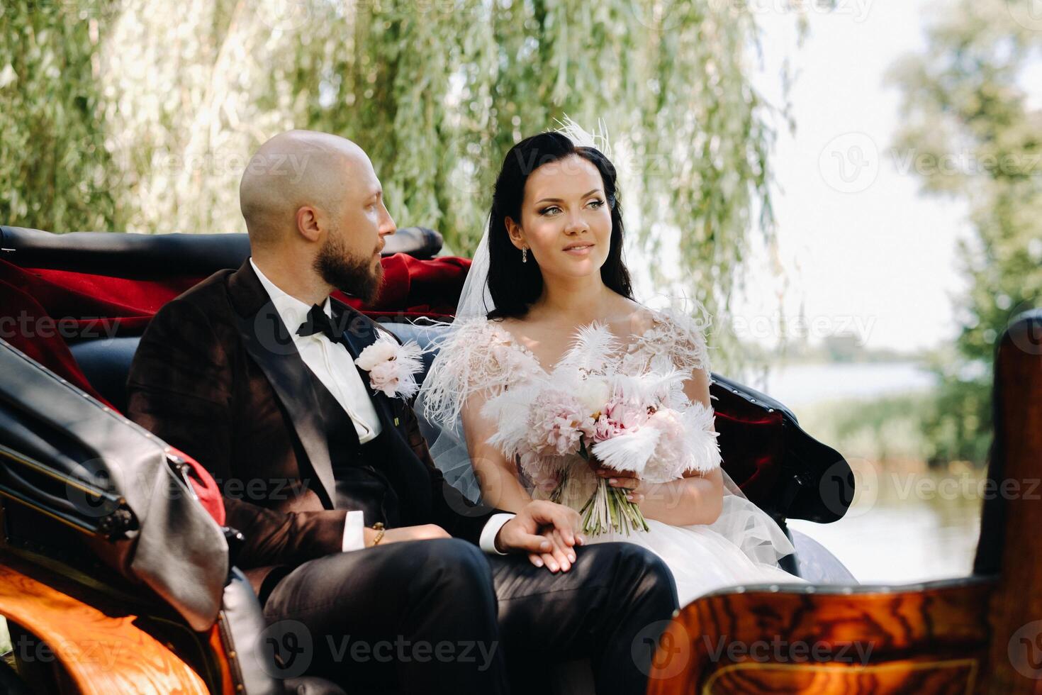 The bride and groom with a bouquet are sitting in a carriage in nature in retro style photo