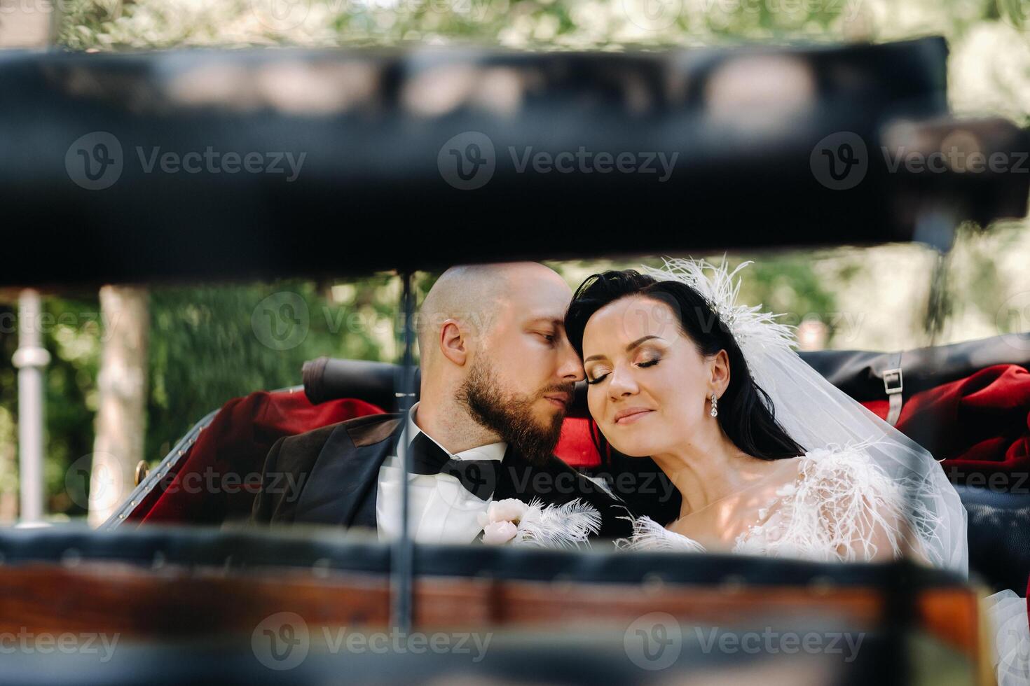 The bride and groom with a bouquet are sitting in a carriage in nature in retro style photo