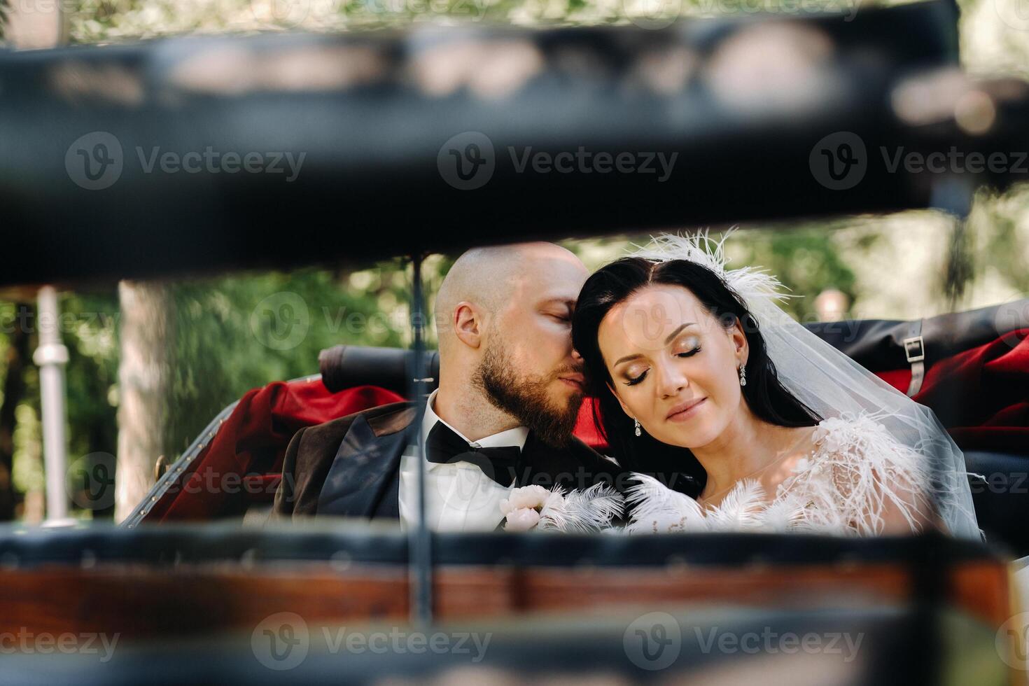 The bride and groom with a bouquet are sitting in a carriage in nature in retro style photo