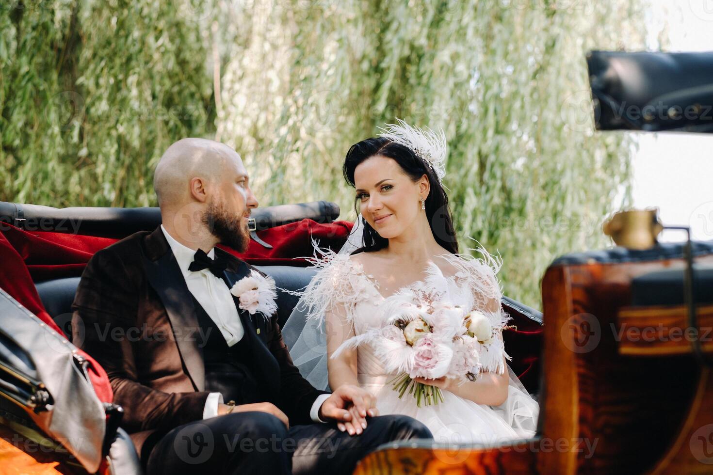 The bride and groom with a bouquet are sitting in a carriage in nature in retro style photo
