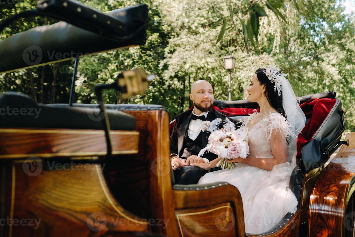 The bride and groom with a bouquet are sitting in a carriage in nature in retro style photo